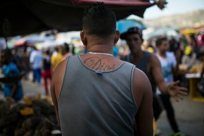 Un trabajador que tiene tatuado en la espalda la palabra "Dios" habla con un cliente en su puesto de verduras en un mercado mayorista de alimentos