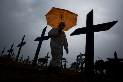Un trabajador vestido con un traje protector y con un paraguas camina frente a las tumbas de las víctimas del Covid-19 en el cementerio de Nossa Senhora Aparecida, en Manaus, Brasil, el 25 de febrero de 2021