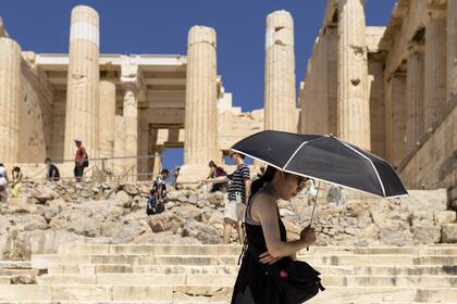 Un turista camina bajo un paraguas durante su visita a la Acrópolis de Atenas el 18 de junio de 2024, Grecia, Atenas