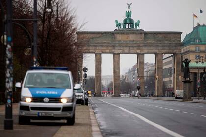 Un vehículo policial patrulla el vacío bulevar de la calle 17 de junio que conduce a la histórica Puerta de Brandeburgo