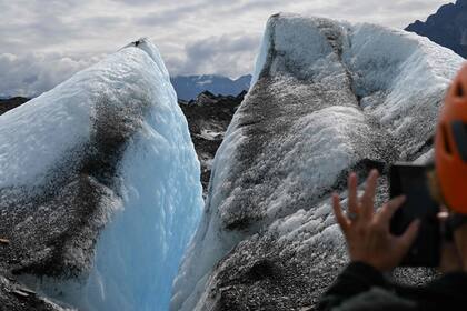 Un visitante toma fotografías del hielo azul en una grieta mientras camina sobre el hielo durante una visita guiada