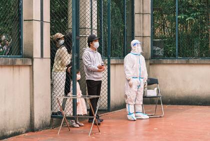 Un voluntario de la comunidad (derecha) que usa equipo de protección personal se para junto a los residentes durante una prueba del coronavirus Covid-19 en un complejo durante una cuarentena en el distrito de Pudong en Shanghái el 19 de abril de 2022