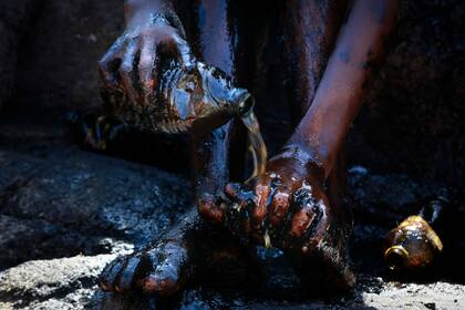 Un voluntario limpia sus manos y pies, manchados con petróleo derramado en las playas de Itapuama, Brasil