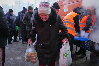 Una anciana carga bolsas en un punto de distribución de alimentos calientes durante un apagón en Kiev