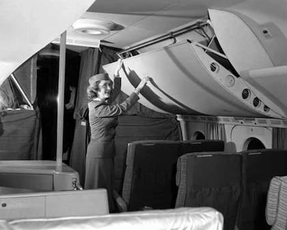 Una azafata armando las literas ubicadas sobre los asientos, en el avión Boeing 377 Stratocruiser
