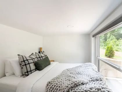 Una cama blanca con almohadones mullidos frente a una gran ventana que da al patio trasero
