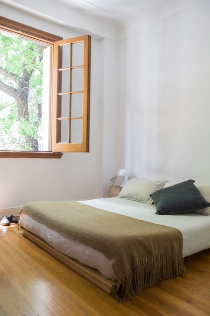 Una cama tipo tatami y no mucho más en este dormitorio con piso de madera, aberturas de época y vista a la copa de los árboles