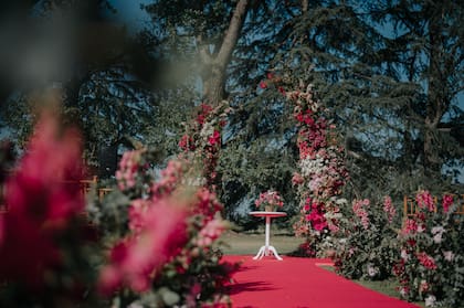 Una ceremonia con dos tótems enormes repletos de flores, un camino color fucsia y canteros de flores hacia ambos lados.