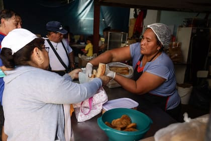 Una de las cocineras de "Olla Talleres" entrega pan y polenta en el comedor de La Dignidad en el barrio de Parque Chacabuco.