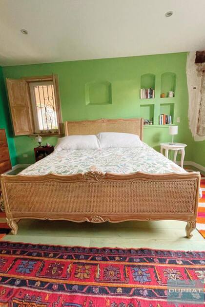 Una de las suites, con cama provenzal con respaldo de esterilla y alfombras coloridas.