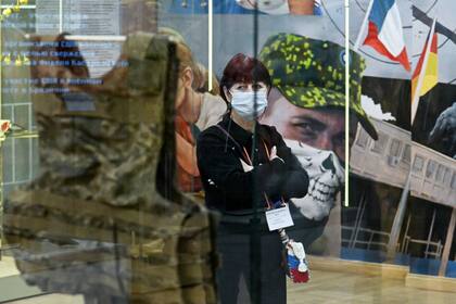 Una empleada del museo de pie junto a una vitrina donde se exhibe un chaleco antibalas