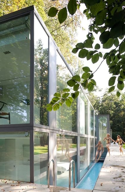 Una fachada de vidrio transparente se abre a un jardín sombreado por árboles y baña el interior con luz natural