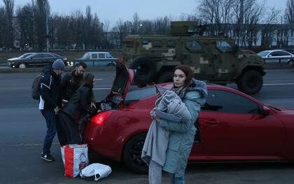 Una familia carga sus cosas en el auto al paso de un vehículo militar en Kiev, en medio de la estampida de refugiados que huyen de la guerra