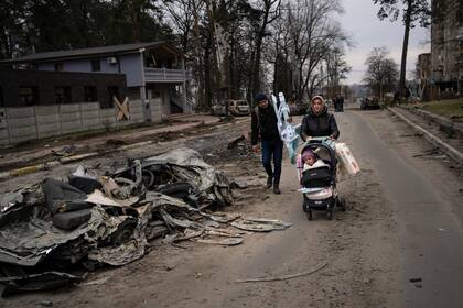 Una familia pasa junto a un automóvil aplastado por un tanque ruso en Bucha, en las afueras de Kiev 