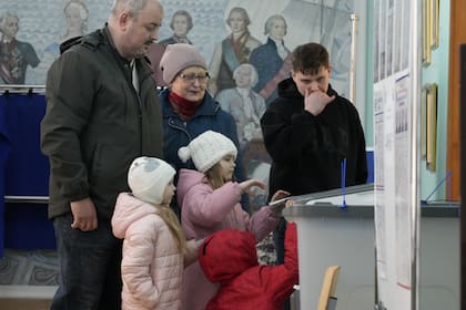 Una familia vota en un colegio electoral ubicado en una escuela durante las elecciones presidenciales en San Petersburgo, Rusia, el sábado 16 de marzo de 2024, con una pintura que representa a la zarina rusa Catalina II y sus contemporáneos en la pared. (AP/Dmitri Lovetsky)