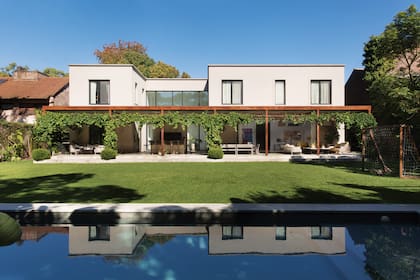 Una foto de la fachada posterior de la casa, donde se ve la pileta, el gran jardín y la galería.