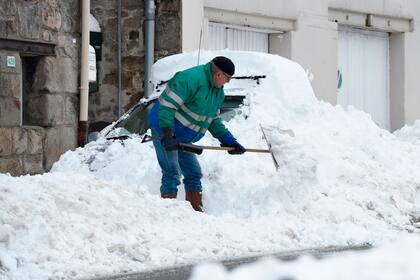 Un hombre quita una densa capa de nieve que cubrió su auto