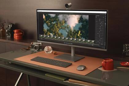 Una HP Envy todo en uno con pantalla de 34 pulgadas. La base del monitor sirve de sistema de carga inalámbrica para un smartphone
