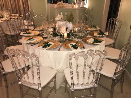 Una imagen de la mesa principal, decorada con rosas blancas nacionales, follaje natural, velas, candelabros con monitos de bronce y sillas modelo Napoleón transparentes.