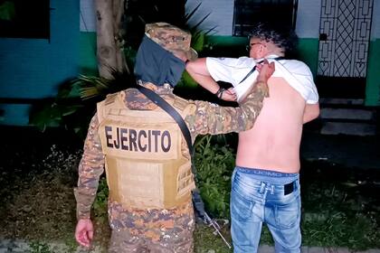 Una imagen difundida por la oficina de prensa de la Presidencia de El Salvador muestra a un soldado revisando el cuerpo de un hombre en busca de tatuajes durante una operación de búsqueda de pandilleros en Soyapango, El Salvador, el 3 de diciembre de 2022.
