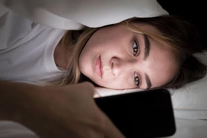 Una joven con su celular al acostarse en la cama