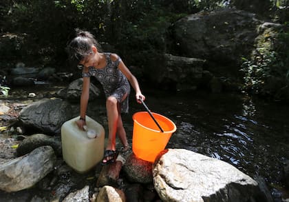 Una joven trata de llevar agua en bidones, recogida de un arroyo del parque nacional