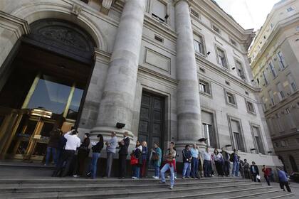 Una larga fila de personas espera ante las puertas de un banco oficial, en la ciudad de Buenos Aires