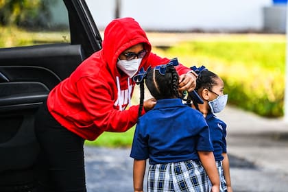 Una madre ajusta la mascarilla a su hija para entrar a la escuela, en Miami (Photo by CHANDAN KHANNA / AFP)
