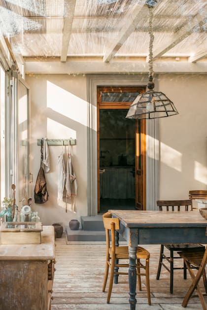 Una mesa de madera vintage, sillas de distinto modelo pero mismo estilo y un cielo rado transparente.