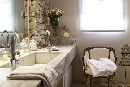 Una mesada de mármol blanco con bacha de una sola pieza y grifería de primera calidad, para acompañar el revestimiento de piedra, protagonista de este baño.