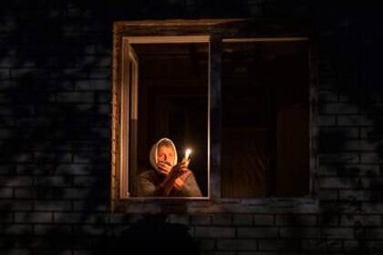 Una mujer alumbra con una vela desde su ventana ante los cortes de electricidad en Ucrania