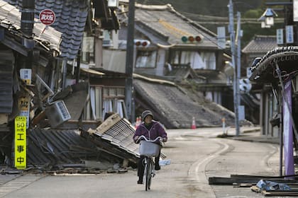 Una mujer anda en bicicleta entre casas dañadas en la ciudad de Noto, en la península de Noto frente al Mar de Japón, el martes 2 de enero de 2024, tras el mortal terremoto del lunes.
