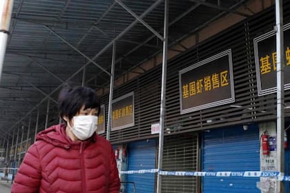 Una mujer camina frente al mercado mayorista de mariscos de Huanan, que fue cerrado por un tiempo y donde las autoridades dicen que se originó el primer brote de la enfermedad respiratoria en Wuhan