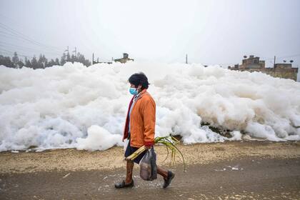 Una mujer camina junto a la espuma tóxica en el barrio Los Puentes. (Photo by Juan BARRETO / AFP)