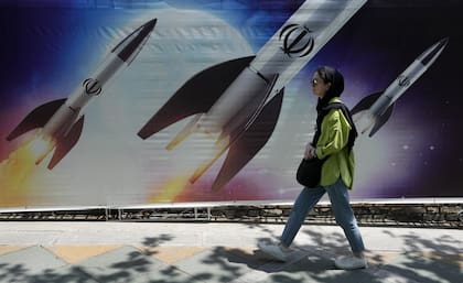 Una mujer camina junto a un cartel que muestra misiles siendo lanzados en el norte de Teherán, Irán, el viernes 19 de abril de 2024.