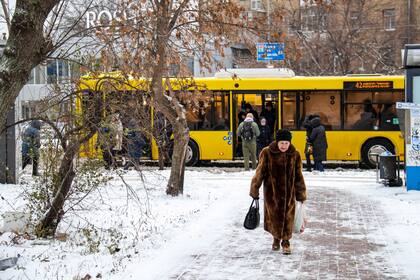Una mujer camina por una calle mientras los viajeros bajan y suben a un autobús durante una nevada en Kiev.
