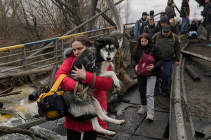 Una mujer carga a su perro mientras cruzan el río Irpín por un puente improvisado para huir de la violencia en Ucrania, el sábado 5 de marzo de 2022. (Foto AP/Vadim Ghirda)