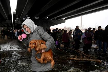 Una mujer carga un perro para cruzar un puente destruido mientras se evacua la ciudad de Irpin, al noroeste de Kiev