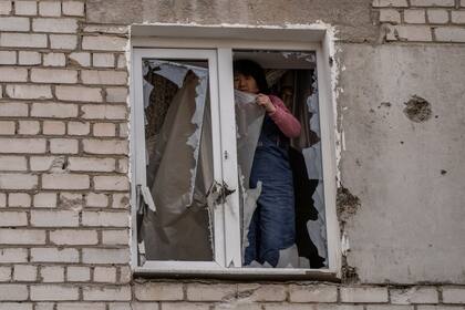 Una mujer coloca un plástico sobre los vidrios rotos de una ventana tras un ataque ruso en la víspera, en la zona residencial de Mikolaiv, Ucrania, el 29 de marzo de 2022. 