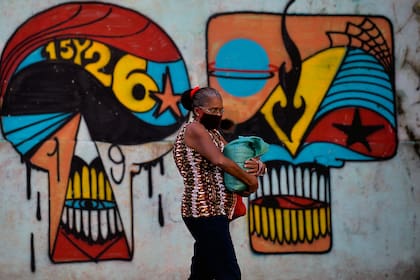 Una mujer con mascarilla camina junto a un mural en La Habana, Cuba