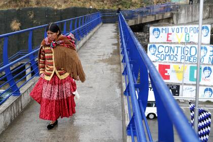 Una mujer cruza un puente con una pared pintada con propaganda política en apoyo del presidente Evo Morales al fondo, en El Alto, Bolivia