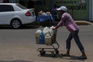Una mujer empuja un carrito cargado con botellas de agua recolectadas de un grifo improvisado en una calle de Maracaibo, Venezuela, el 25 de mayo de 2020 durante la pandemia del coronavirus