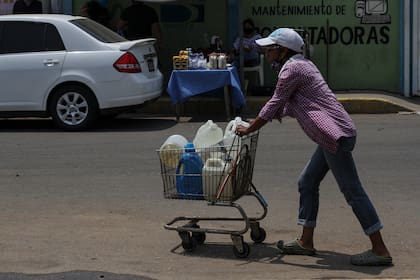 Una mujer empuja un carrito cargado con botellas de agua recolectadas de un grifo improvisado en una calle de Maracaibo, Venezuela, el 25 de mayo de 2020 durante la pandemia del coronavirus