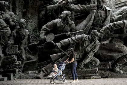 Una mujer empuja un cochecito de bebé mientras pasan junto a esculturas en bajorrelieve que representan escenas de guerra en el Museo Nacional de Historia de Ucrania durante la Segunda Guerra Mundial en Kiev, Ucrania, el lunes 8 de abril de 2024.
