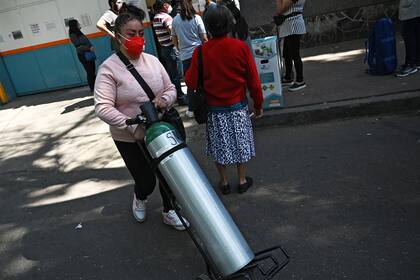 Una mujer transporta su tanque con ruedas afuera de un centro de carga en México