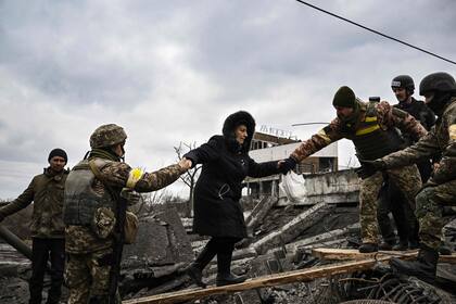 Una mujer es asistida por militares ucranianos mientras la gente cruza un puente destruido mientras evacuan la ciudad de Irpin, al noroeste de Kiev, durante fuertes bombardeos y bombardeos el 5 de marzo de 2022