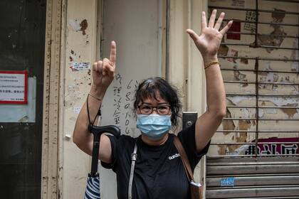 Una mujer hace un gesto con el lema de protesta a favor de la democracia mientras la policía patrulla el área después de que los manifestantes convocaron una manifestación en Hong Kong