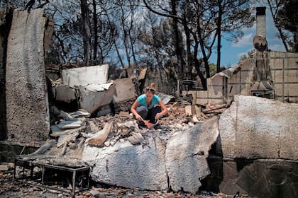 Una mujer intenta encontrar sus pertenencias debajo de los escombros de su casa quemada después de un incendio forestal en el pueblo de Neos Voutzas, cerca de Atenas
