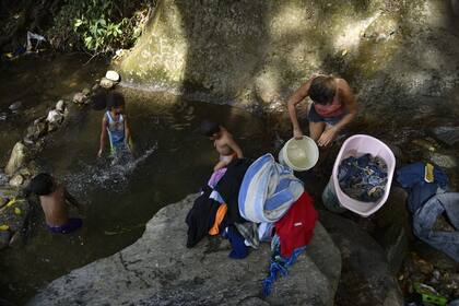 Una mujer lava la ropa mientras sus hijos juegan en una zona de aguas calmas, en el Parque Nacional El Ávila