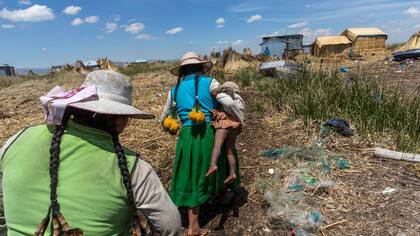 Una mujer lleva a su bebé camino a su casa en Kapi Cruz Grande, una aldea en las orillas llenas de basura del Lago Titicaca en la región de Puno en Perú